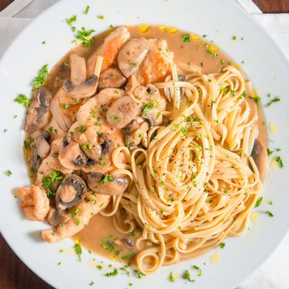 Chicken and mushrooms in a creamy sauce with linguine pasta, garnished with parsley.
