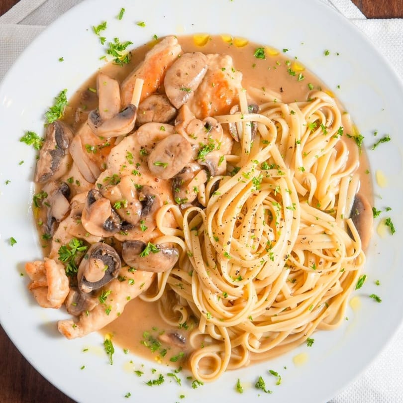 Chicken and mushrooms in a creamy sauce with linguine pasta, garnished with parsley.